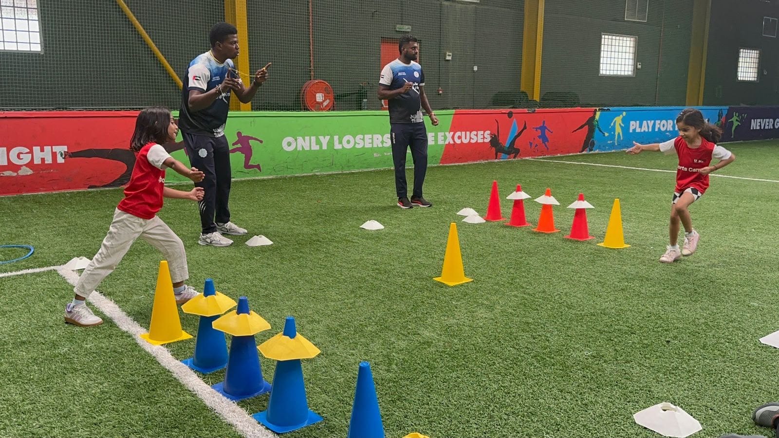 Coaches leading children through a cone relay game during an indoor Wolf Kids P.E session