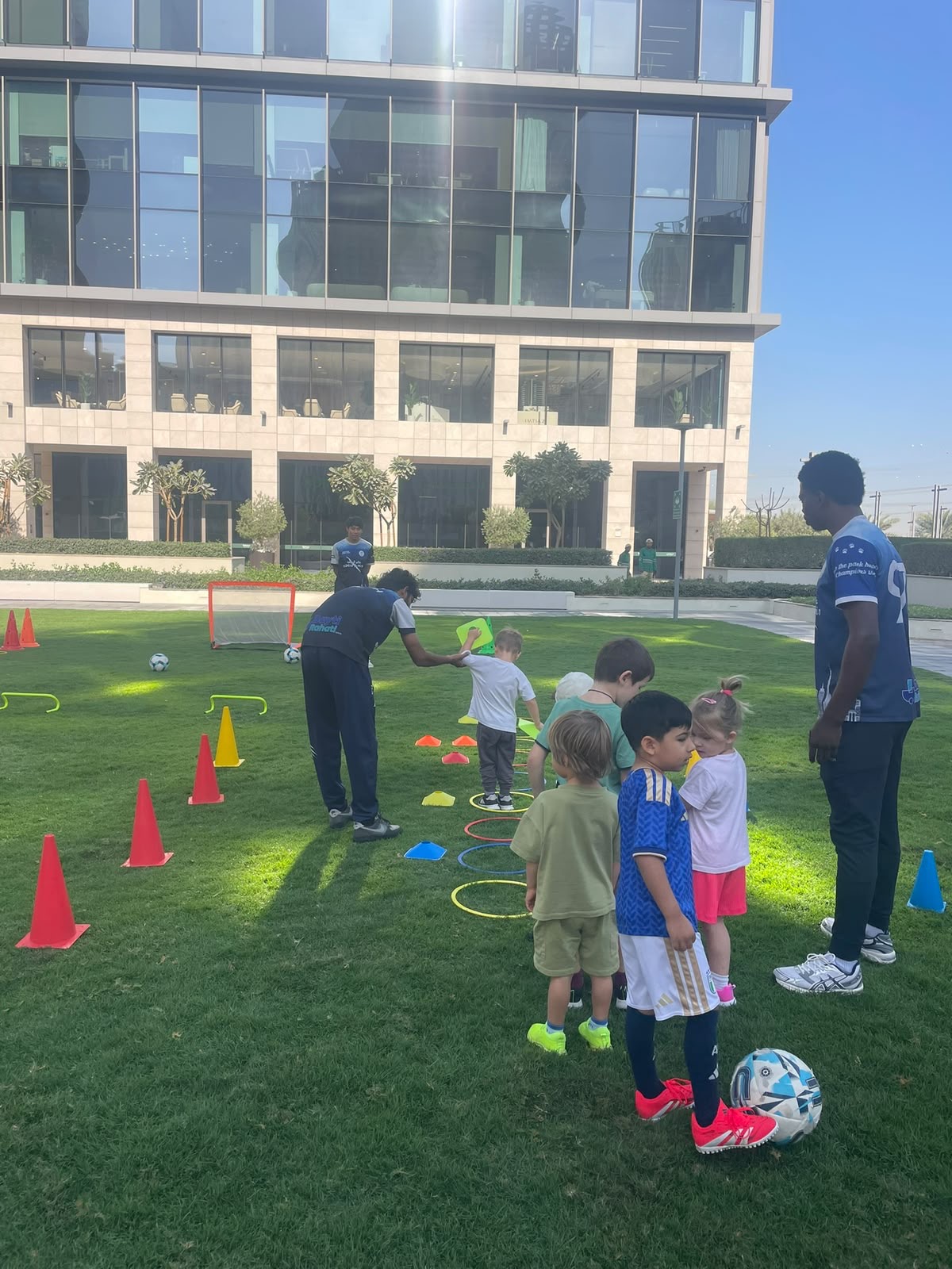 A Wolf Kids coach guiding a child with a football on a grass park in Dubai.